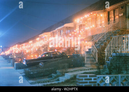 Les lumières de Noël sur les maisons et les voitures garées dans l'entrée de la maison de banlieue en 1965 Banque D'Images