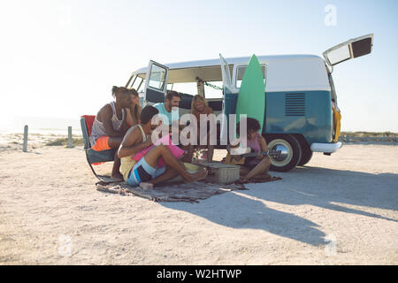 Groupe d'amis s'amusant près de camping-van at beach Banque D'Images