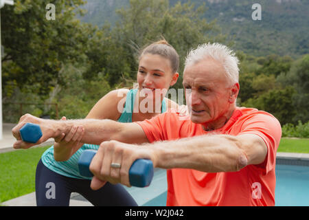 Entraîneur féminin senior actif aidant à exercer avec haltères Banque D'Images