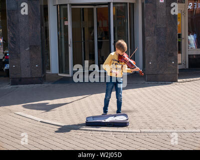 Riga, Lettonie - Juin 14, 2019 : Little Boy with pull jaune violine à jouer dans la zone piétonne de Riga Banque D'Images