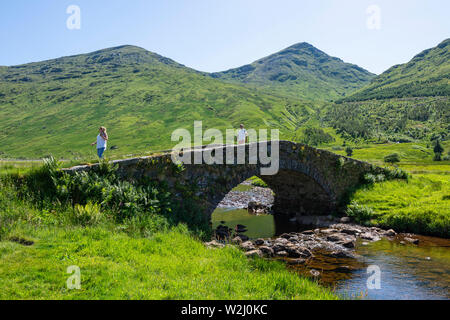 Touristes traversant Butterbridge, un vieux pont voûté unique en pierre, plus Kinglas Kinglas dans de l'eau Glen, Argyll and Bute, Ecosse, Royaume-Uni Banque D'Images