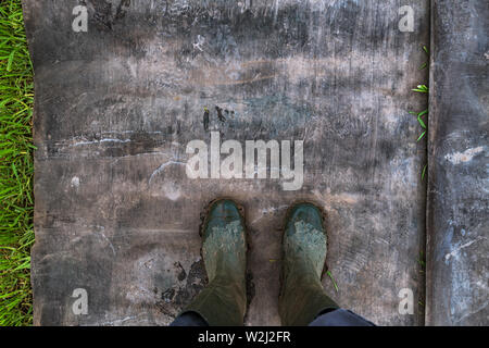 Vue du dessus de l'agriculteur portant des bottes en caoutchouc sale après une marche à travers champ boueux Banque D'Images