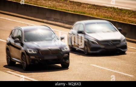 Un véhicule chaque par BMW et Mercedes-Benz dur à grande vitesse les unes à côté des autres sur une autoroute Banque D'Images