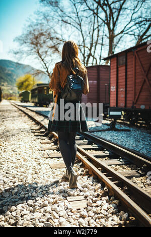 Une belle jeune femme avec un sac à dos sur son dos est à pied par un chemin de fer près de la charrette, l'attente d'un train. Vue arrière. Banque D'Images