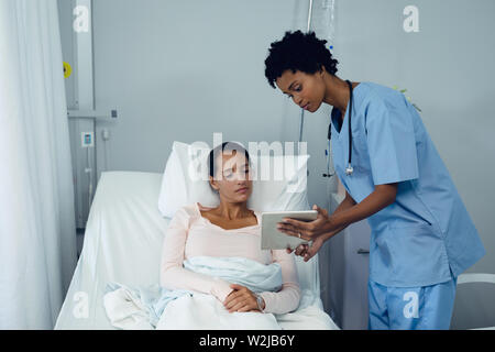 Femme médecin montrant rapport médical à female patient on digital tablet dans le ward Banque D'Images
