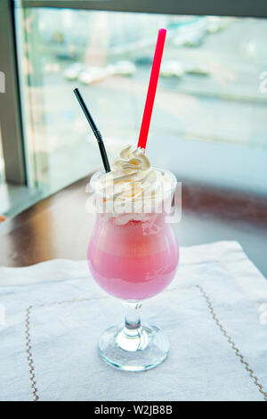 Verre de lait fouetté aux fraises avec de la crème chantilly de couleur rose. Beau fruit sucré cocktail sur la table dans le restaurant Banque D'Images
