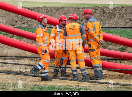 09 juillet 2019, Basse-Saxe, Burgdorf : les travailleurs de la construction sont debout sur un site de construction en face de conduites vides pour câbles de masse. Les premiers tests Tennet charrue multiples pour pose en trois phases 380 kV câbles de masse. Photo : afp/Riechau Cindy Banque D'Images