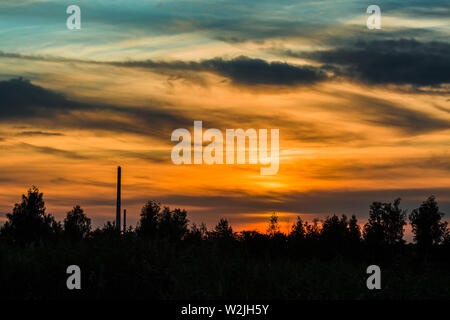 Dramatique sombre avec les nuages ciel coloré après le coucher du soleil. Black horizon avec des arbres et une cheminée. Soir d'été, paysage. Banque D'Images