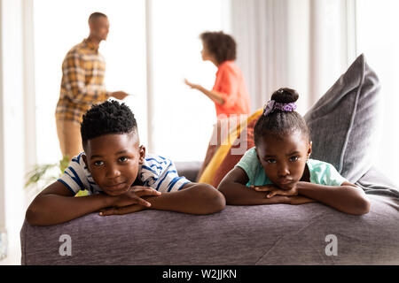 Bouleversé les enfants assis sur un canapé pendant que leurs parents se disputer dans l'arrière-plan Banque D'Images