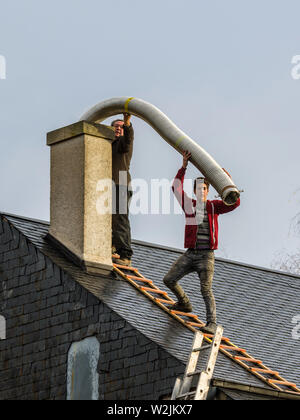 Deux hommes sans équipement de sécurité sur le toit de la chambre de combustion montage en cheminée - France. Banque D'Images