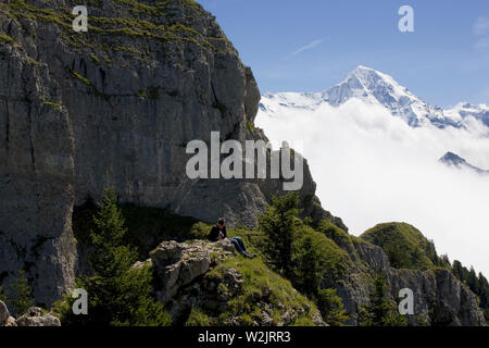 Randonneur repose sur Schynige Platte, avec la masse de l'Gumihorn à gauche et le sommet enneigé du Mönch au-delà : Oberland Bernois, Suisse Banque D'Images