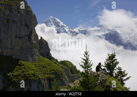 Randonneur repose sur Schynige Platte, avec la masse de l'Gumihorn à gauche et le sommet enneigé du Mönch au-delà : Oberland Bernois, Suisse Banque D'Images