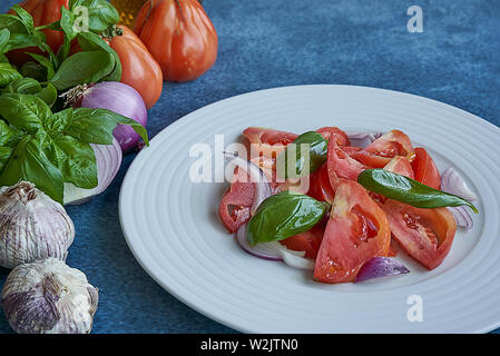 Salade de tomates légumes avec l'huile d'olive extra vierge, de l'oignon violet pourpre, l'ail et le basilic. Accompagné d'une bouteille d'huile d'olive extra vierge, violet o Banque D'Images