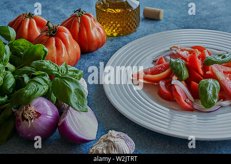 Salade de tomates légumes avec l'huile d'olive extra vierge, de l'oignon violet pourpre, l'ail et le basilic. Accompagné d'une bouteille d'huile d'olive extra vierge, violet o Banque D'Images