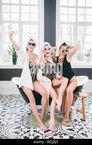 Photo montrant groupe des amis heureux à spa. les filles avec des serviettes sur la tête s'amusant et en prenant à la maison selfies. Amitié, cosmétique, slumber party co Banque D'Images