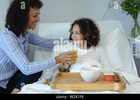 L'alimentation de la mère son fils le jus d'orange dans le lit dans l'ward Banque D'Images