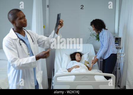 Male doctor examining x-ray rapport tandis que mère tenant son fils mains dans la paroisse Banque D'Images