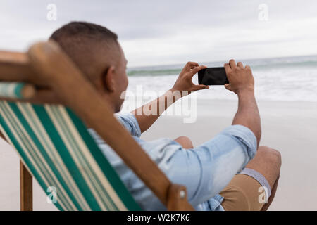 Photos cliquer sur l'homme avec un téléphone mobile tout en restant assis sur une chaise de plage Banque D'Images