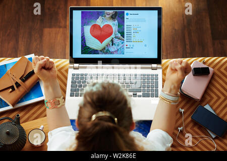 Vue supérieure de la femme au foyer à la mode sourire assis sur le divan dans le salon moderne de travailler sur les médias sociaux compte. Banque D'Images
