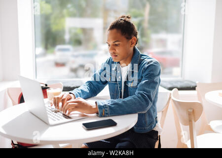 Si sérieux. Homme concentré passer du temps dans un café et de taper un message sur son ordinateur portable Banque D'Images