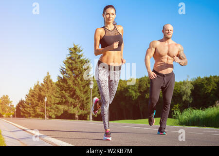 Les jeunes hommes et femmes forts modèles de remise en forme en plein air dans le magnifique paysage. L'homme et de la femme en marche dans le parc au coucher du soleil Banque D'Images