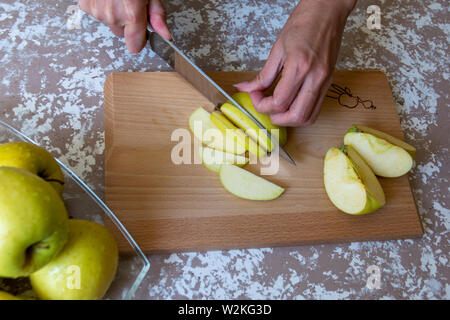 Coupe Femme au couteau une pomme à tranches sur une planche à découper sur une table dans la cuisine. Pommes Chantecler. La cuisson des aliments. Banque D'Images