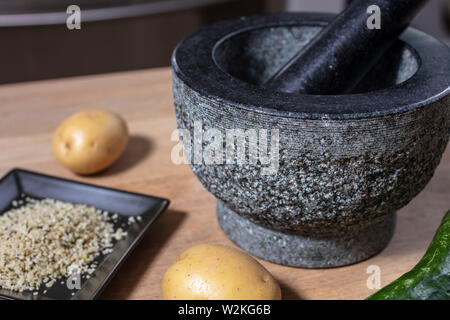 Mortier et pilon en pierre sur un comptoir de cuisine avec pomme de terre, les graines de chanvre et de concombre Banque D'Images
