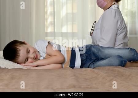 Le médecin s'assoit sur le bord du lit, à côté d'un sourire, faire semblant de dormir l'enfant. Banque D'Images