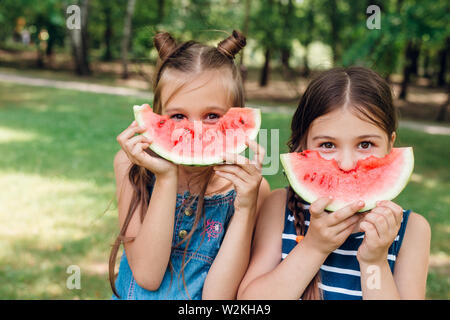Deux mignonnes petites filles eating watermelon et s'amuser dans le parc en été Banque D'Images