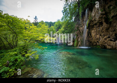 L'eau d'un petit ruisseau s'engouffre dans la roche dans l'eau couleur azure d'un étang au parc national des Lacs de Plitvice en Croatie Banque D'Images