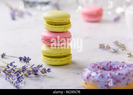 Trois macarons et branches de lavande en centre de l'image, un donut dans lilas avant, un macaron derrière, sur la table de marbre blanc Banque D'Images