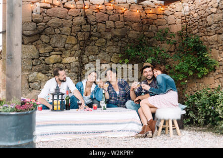 Portrait of happy young people sitting ensemble et rire tout en profitant d'une soirée avec des cocktails sur la table. Banque D'Images