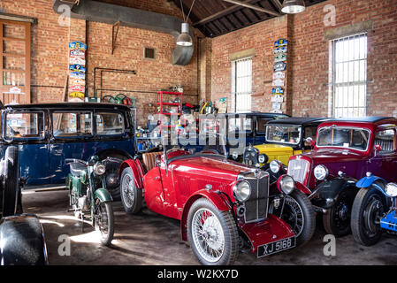 Voitures anciennes dont une rare 1923 MG J2 Midget et Austins garé dans un garage à Bicester Heritage, UK Banque D'Images