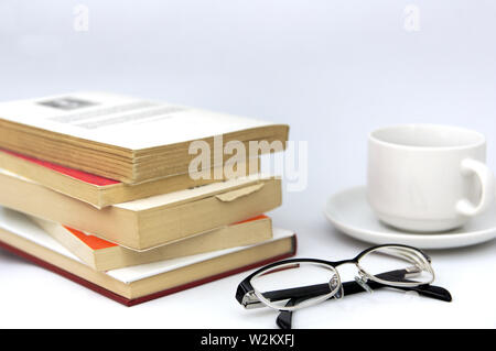 Une table avec beaucoup de livres, à côté d'eux une tasse de café et des lunettes de lecture Banque D'Images