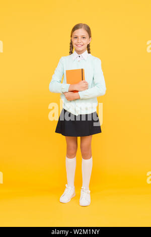 Une base de connaissances pour l'avenir. Adorable petite fille tenant livre sur fond jaune. Enfant mignon petit livre avec la connaissance dans les mains. Connaissances et compétences. Jour des connaissances ou le 1 septembre. Banque D'Images