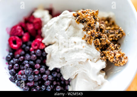 Gros plan macro de bol de crème glacée à la vanille garnie de bleuets congelés myrtilles et petits fruits rouges framboises granola Banque D'Images