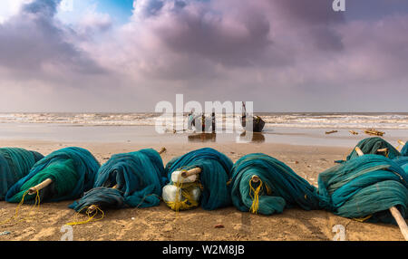 Les filets de pêche au bord de la mer avec vue sur les pêcheurs qui luttent pour remorquer leurs bateaux à la mer. Banque D'Images