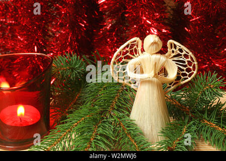 Ange priant dans les branches d'arbre de Noël avec une bougie rouge et chaînes scintillants Banque D'Images