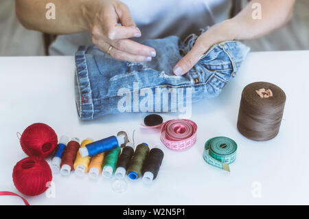 Women's Hands, un tailleur coud des vêtements à une table sur laquelle se trouvent des bobines de fil Banque D'Images