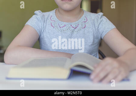 Torturé petite fille lit un livre à la table et elle est très fatiguée et veut dormir, bâillements, s'endort pendant que lire des histoires et leçons Banque D'Images