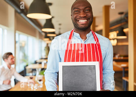 Smiling waiter holding est un tableau noir craie comme serveuse au restaurant ou bar Banque D'Images