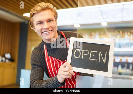 Jeune homme qu'un restaurant fondateur montre un tableau avec le lettrage Ouvrir Banque D'Images