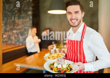 Jeune homme servant de waiter serving salade grecque au restaurant Banque D'Images