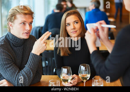 Jeune couple à l'alimentation des commandes serveur avec bloc-notes de restaurant ou de bistro Banque D'Images