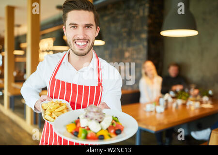 Jeune serveur servant de restaurant comme salade grecque à la feta apéritif Banque D'Images