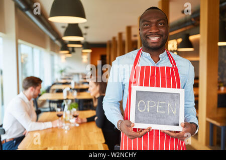 Smiling waiter holding est une craie tableau noir avec les écritures ouvrir comme un service d'informations Banque D'Images