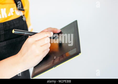 Tablette graphique avec stylet en mains de jeune femme en jaune t-shirt, isolé sur fond gris Banque D'Images