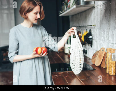 Jeune femme en robe gris pommes tire hors de chiffon tricot chaîne sac shopper Sac dans la cuisine, zéro déchet, slow life Banque D'Images