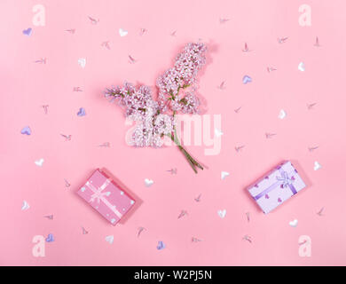 Des brindilles et des fleurs de lilas et de coffrets cadeaux sur fond rose. Banque D'Images