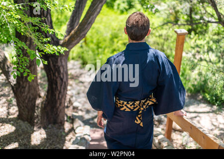 Jeune homme en costume kimono walking back holding sur main courante clôture dans un jardin extérieur au Japon avec la nature vue vers le bas Banque D'Images